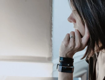 Profile of a person with short dark hair, resting chin on hand, looking at a monitor displaying code.