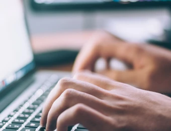 Close-up of hands typing on a laptop keyboard.