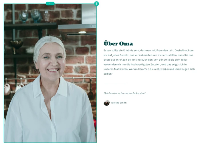 Smiling woman with white hair in a white blouse, in a kitchen with a brick wall and shelves of jars.