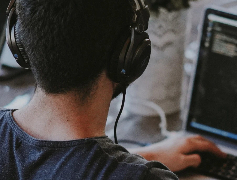 Back view of a person wearing headphones, at a desk with two screens showing code.